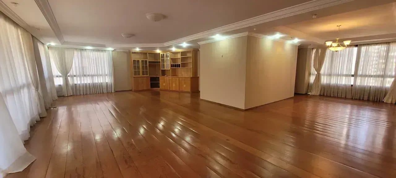 Sala de estar ampla com piso de madeira, armário embutido e grandes janelas com cortinas.