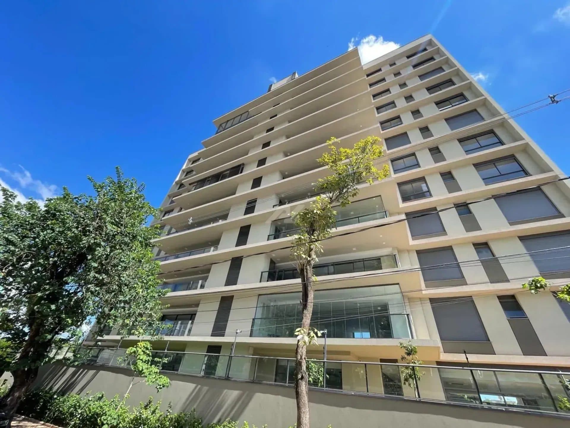 Fachada do edifício residencial contra um céu azul, mostrando varandas e amplas janelas.