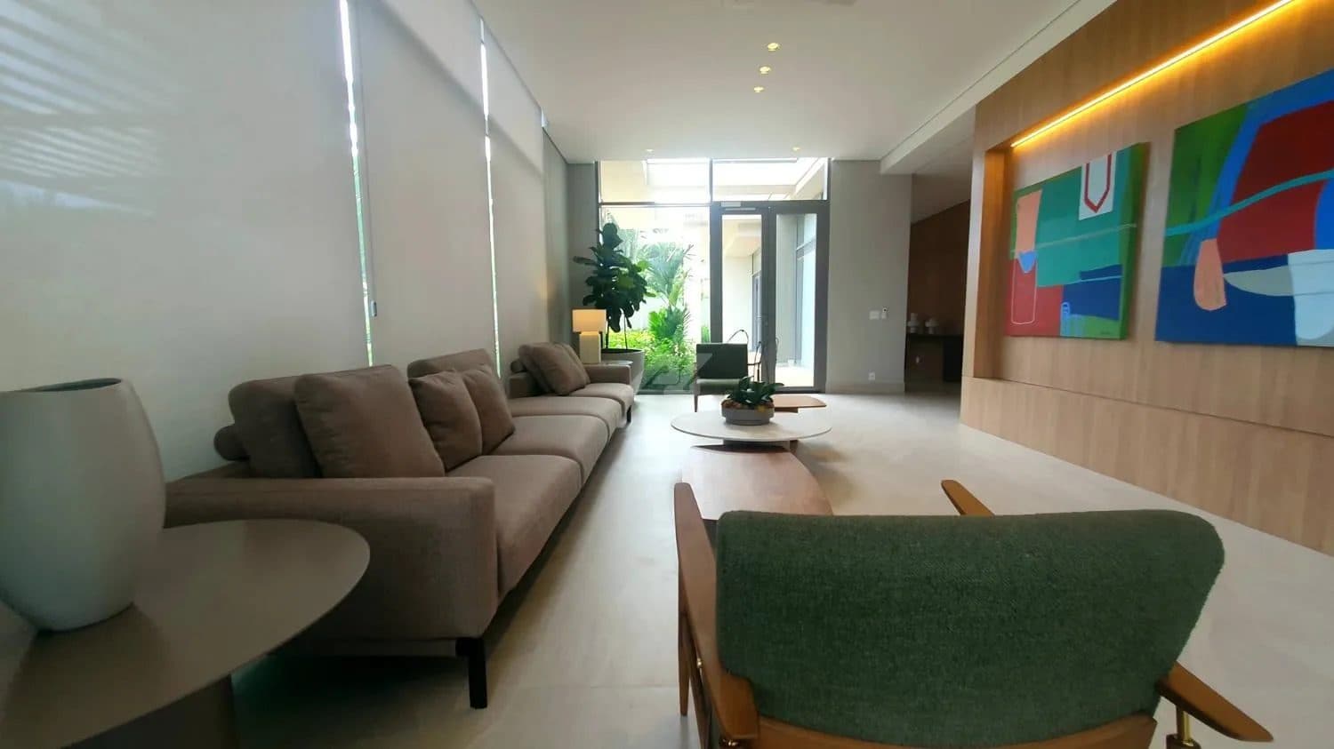 Sala de estar decorada com sofá bege, poltrona verde, mesas de centro e quadros coloridos na parede.